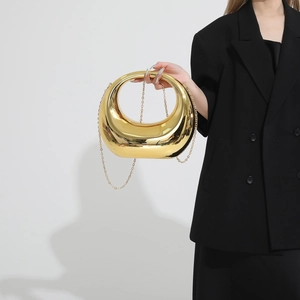 Golden crescent moon hard shell evening bag with chain strap held by a model