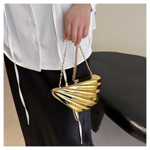 Close-up of gold shell-shaped acrylic clutch bag with metal chain strap on model