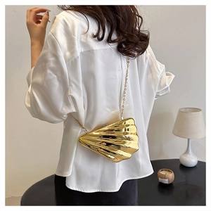 Detail of a golden shell-shaped evening clutch bag with a slim metal chain strap