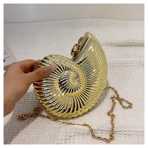 Detail of a golden conch shell evening bag featuring spiral texture and a fine chain strap