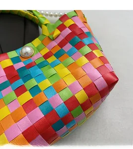 Détail d'un sac tressé multicolore avec bouton perle et bandoulière en perles nacrées
