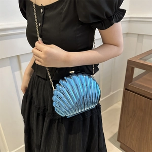 Blue shell-shaped acrylic clutch bag with gold chain strap shown on model's waist