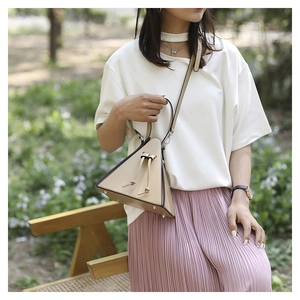 Detail of minimalist beige triangle leather handbag with silver hardware and drawstring knot