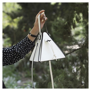 Macro detail of white triangle handbag featuring black edge paint and metal bottom studs