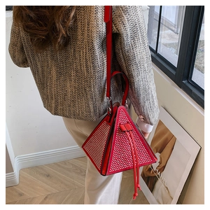 Détail d'un sac à main triangle rouge avec strass porté sur une veste en tweed gris