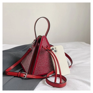 Détail d'un sac triangulaire rouge orné de clous argentés et fermeture éclair en métal