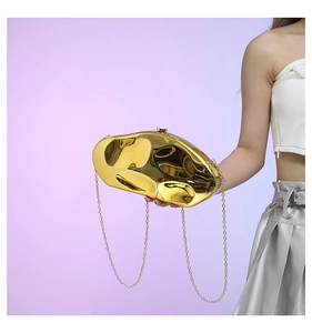 Close-up of golden irregular stone-shaped clutch bag with polished mirror finish and chain