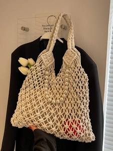 Detail of cream macramé woven tote bag featuring faux pearl handle and chic knit pattern