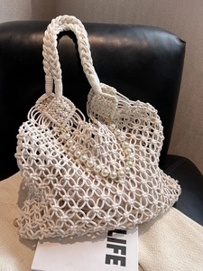 Close-up of white macramé tote bag with woven texture, pearl strap, and beige lining