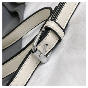 Détail macro de la bandoulière en cuir crème avec bord noir et boucle argentée
