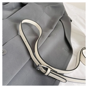 Détail d'une bandoulière réglable en similicuir blanc avec boucle argentée sur tissu gris