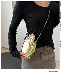 Detail of creative gold hand-shaped acrylic clutch bag with metallic chain on a model