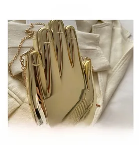 Detailed view of hand-shaped gold metal clutch with chain on beige suit fabric