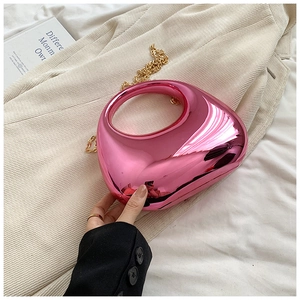 Pink acrylic evening box bag with golden ring handle and chain strap on knit background