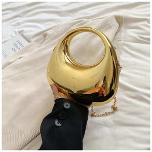 Close-up of golden metallic egg-shaped bag with round hollow handle and fine chain strap