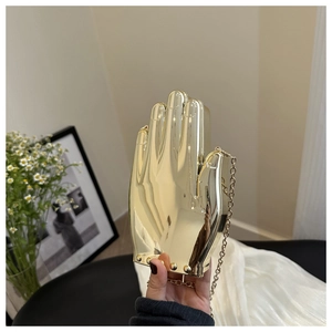Detail of the unique hand-shaped gold acrylic clutch with metallic chain strap