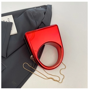 Detail of red acrylic evening bag with circular cutout handle and gold chain on gray suit