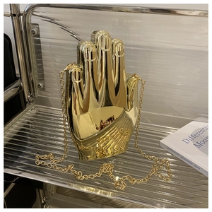 Macro detail of the golden hand-shaped clutch bag with polished metallic finish and chain