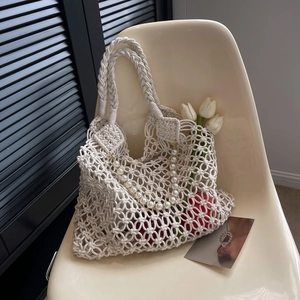 Detail of hollow macrame beach bag in beige with faux pearl chain and tulip decor