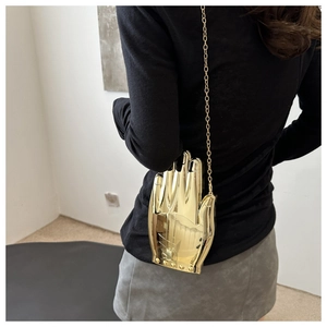 Detail view of the unique gold hand-shaped metal clutch with a sleek chain strap