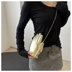 Detail of a gold hand-shaped acrylic clutch bag with a metallic chain strap on a model