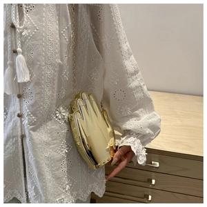 Close-up of golden hand-shaped acrylic clutch bag with metal chain strap worn by model