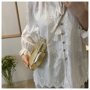 Close-up of a gold palm-shaped acrylic clutch bag held by a model in a white shirt