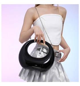 Glossy black crescent handbag with silver chain strap shown on model against a gradient backdrop