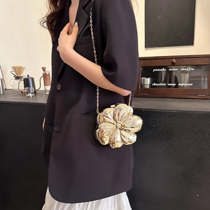 Detailed view of the gold flower-shaped metal clutch with chain strap on a cafe table