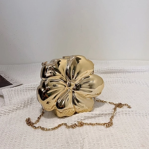 Detail of flower shaped gold metal clutch with mirror finish and delicate chain