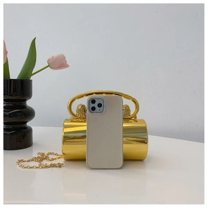 Goldene Zylindertasche mit Löwenrelief und Kettengurt neben einem Handy zum Größenvergleich