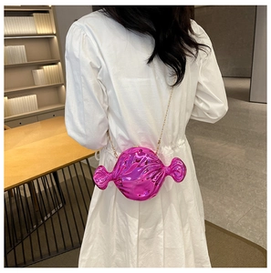 Detail of bright pink candy-shaped crossbody bag with gold chain on white dress