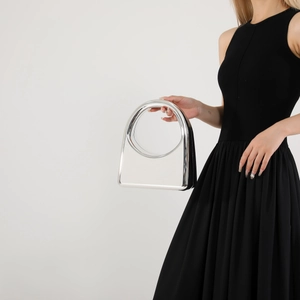 Detail of mirrored silver acrylic handbag showing high-gloss finish and round cutout handle
