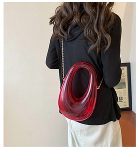 Detailed view of red transparent acrylic oval clutch bag with gold metal chain strap