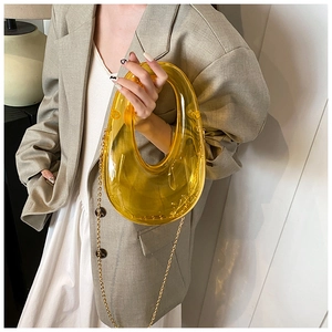 Detail of yellow translucent acrylic clutch bag featuring a gold chain and U-shaped frame