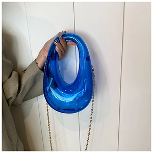 Detail of blue acrylic transparent clutch featuring oval hollow handle and gold chain strap