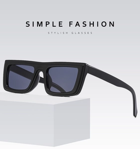 Detail view of bold black rectangular sunglasses with dark lenses on a white pedestal