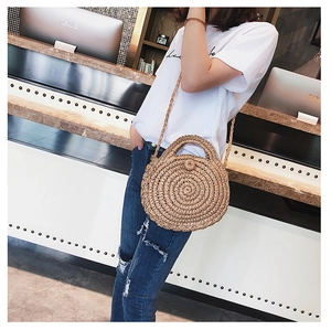 Detail of round handmade straw bag with woven button closure and long shoulder strap