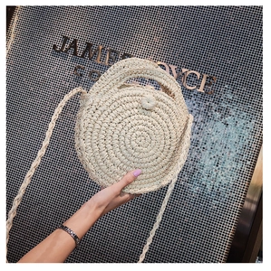 Detail of round straw crossbody bag featuring woven handles and long shoulder strap