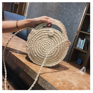 Detail of round straw beach bag featuring spiral woven texture and woven ball button clasp