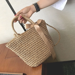 Detail of hand-woven straw bag featuring an elegant champagne silk bow and woven handle