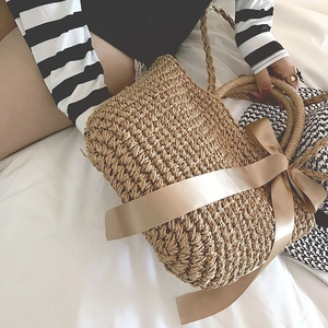 Detail of hand-woven straw bag with large champagne silk bow and round handles