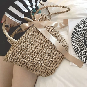 Detail of hand-woven straw bag featuring a large beige satin bow and rope handles