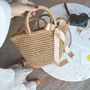 Close-up of handwoven straw bag with a delicate cream silk bow on a marble table