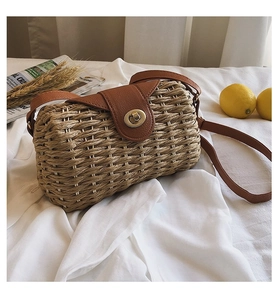 Handmade straw crossbody bag with brown leather flap and golden twist lock on white cloth