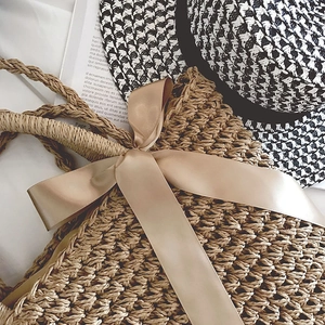 Detail of hand-woven straw bag with satin bow and rope handles for beach vacation
