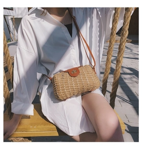 Outdoor shot of a woven straw crossbody bag with brown leather flap and gold lock detail