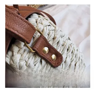 Détail du sac en paille tressée avec bordure en cuir marron et rivets métalliques dorés