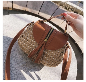 Détail d'un sac en paille tressée avec rabat en cuir marron et pompon doré zippé