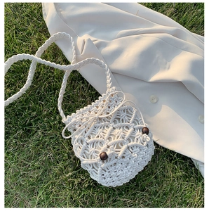 Dettaglio borsa a secchiello intrecciata beige con perline di legno su erba